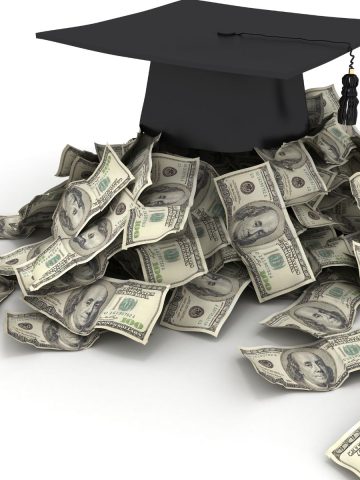 Graduation cap sitting on top of a pile of hundred dollar bills