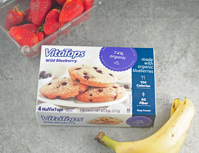 A box of VitaTops width a banana and a plastic container of strawberries.